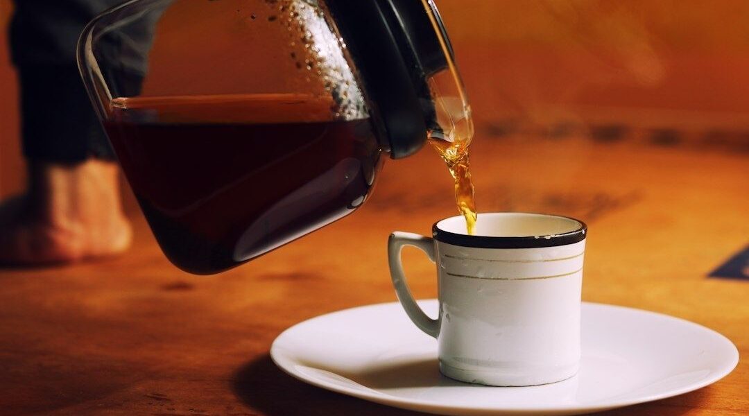 Kaffe hälls från en kanna i en kopp på ett fat