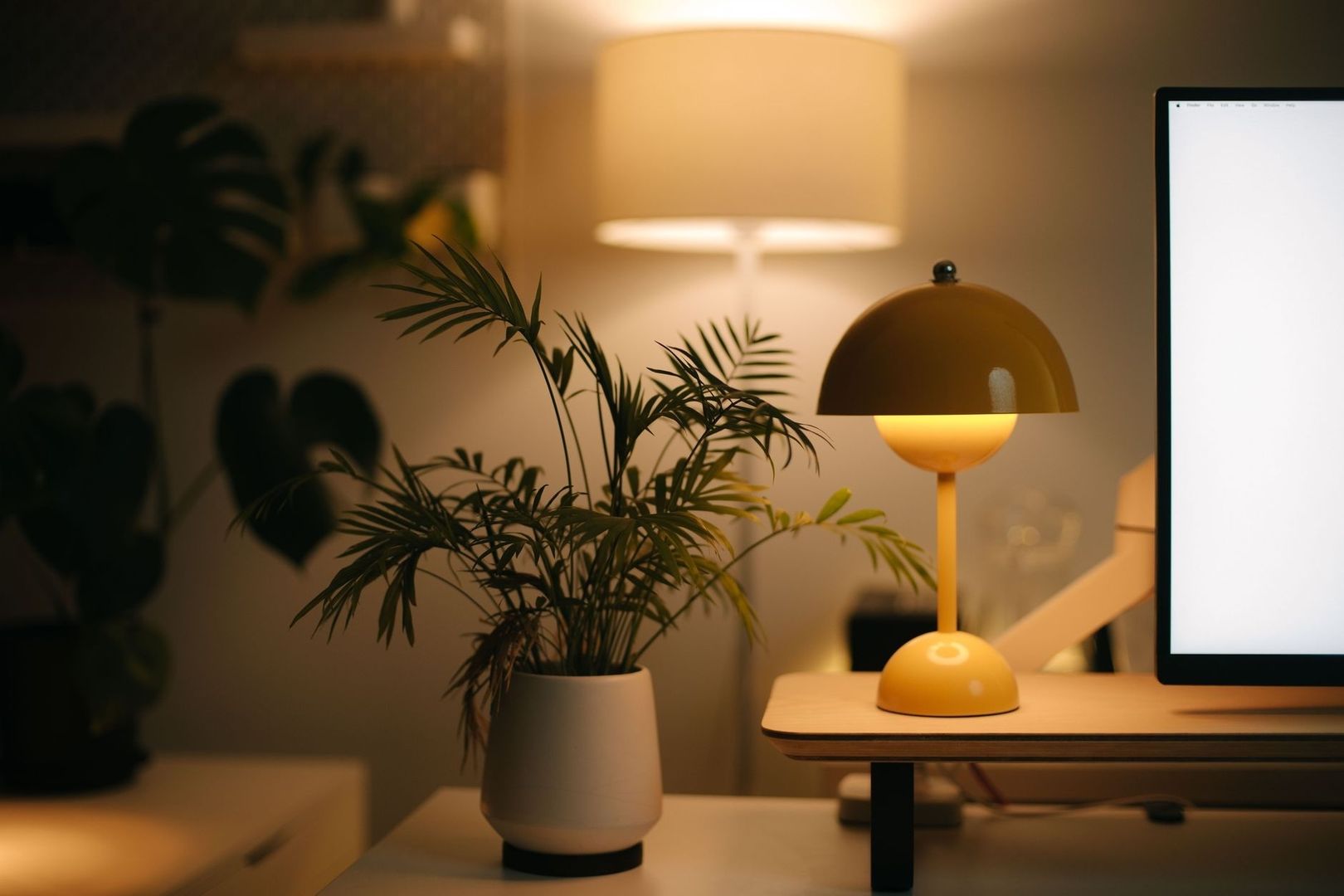 Varmt belyst skrivbord med växt, bordslampa och datorskärm